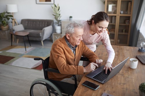 Portrait of senior man in wheelchair using laptop with nurse assisting him.