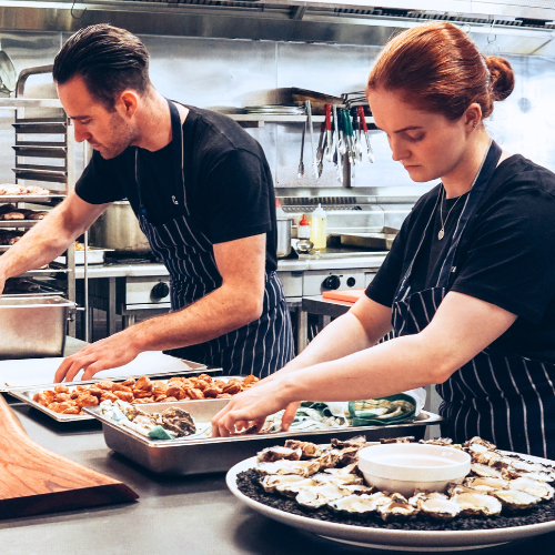 Two people cooking in a professional kitchen.