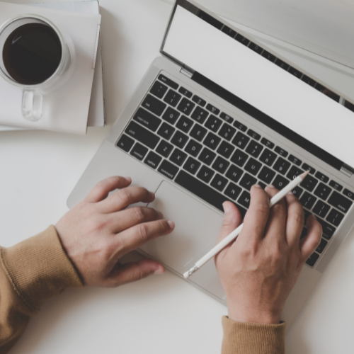 An aerial view of a person holding a pencil while typing on a laptop