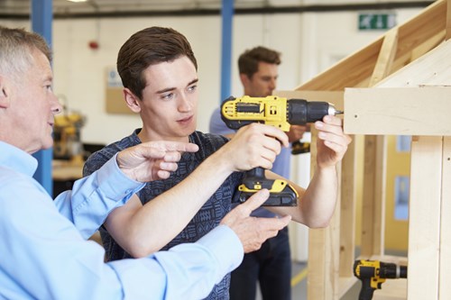 Mentor instructing an apprentice on how to use a drill.