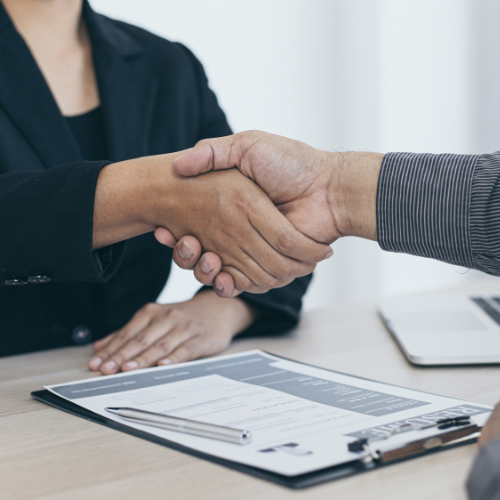 Man and woman shaking hands. A clipboard is on the table.