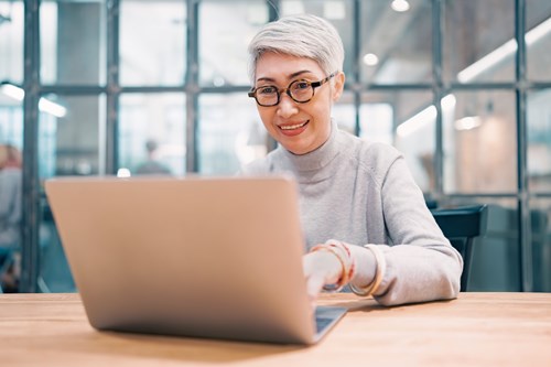 Close-up portrait of smiling middle aged woman using laptop on desk.