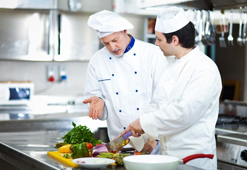 Two Chefs at work in the Kitchen chopping vegetables.