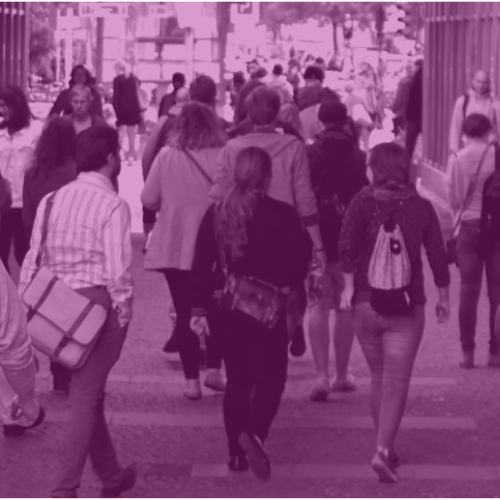 A crowd of people walking down a high street. Image has a purple tint.