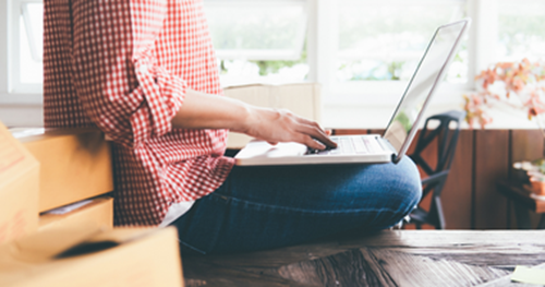 Person sitting on a table with their legs grossed working on a laptop