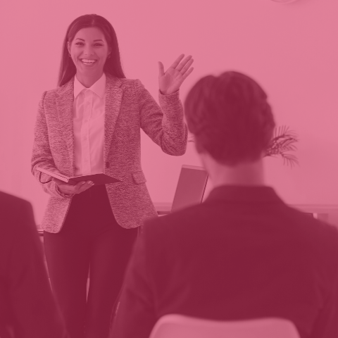 Woman smiling as she presents to a group of people. Image has a red tint.