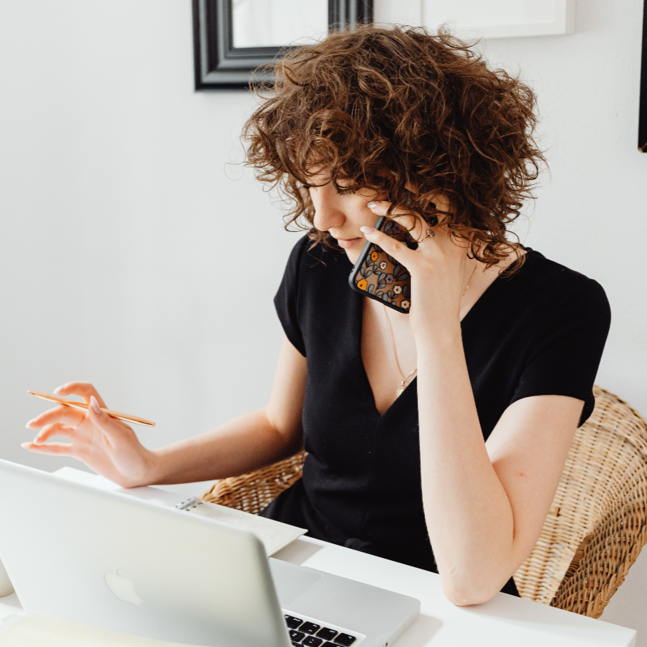 Woman speaking on a mobile phone sitting in front of a laptop.