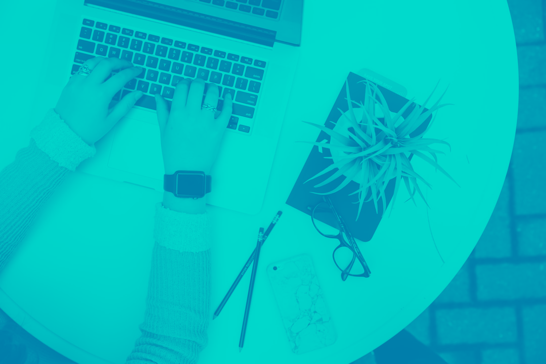 Person typing on a laptop with plant beside her with a blue tint